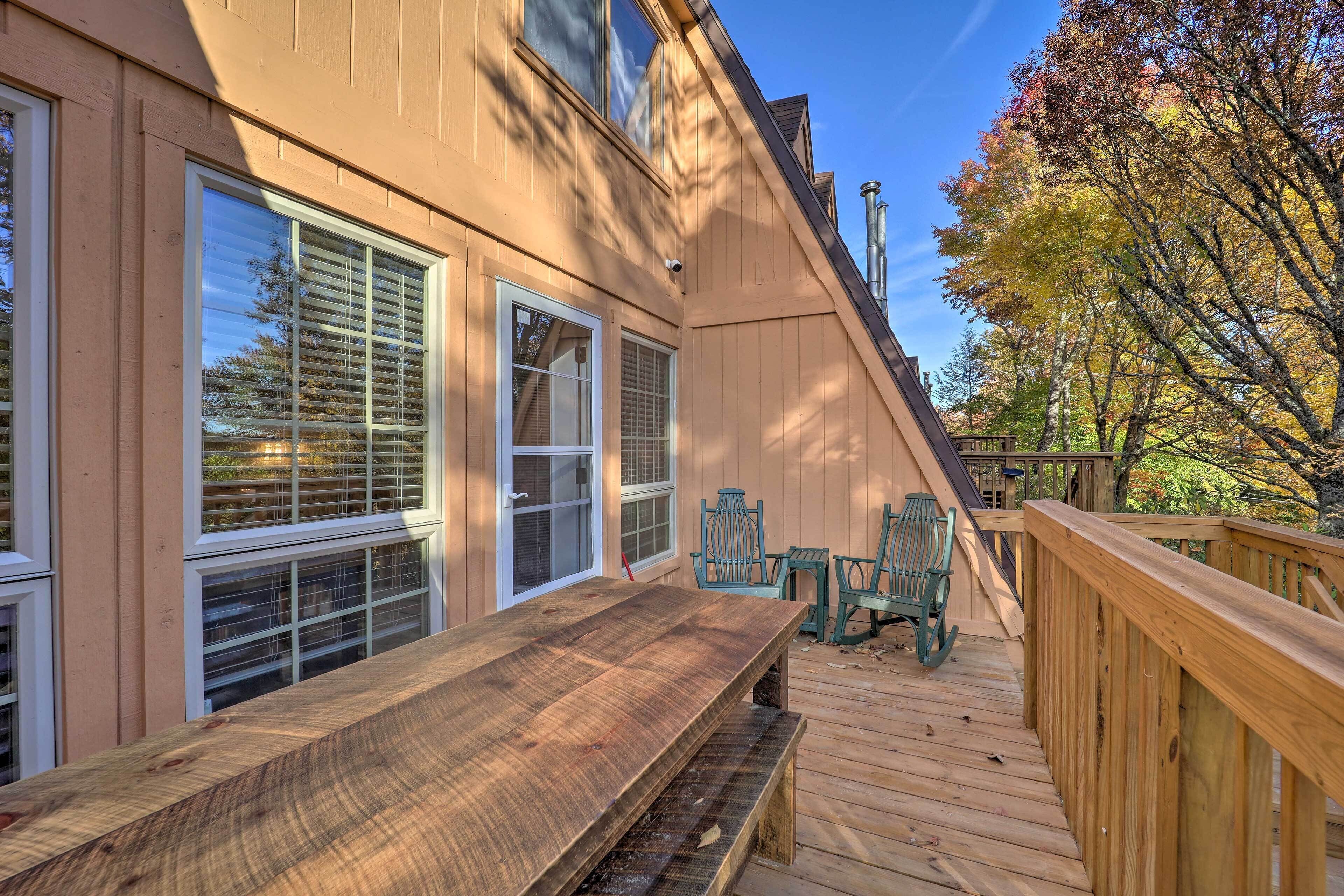 A wooden deck with a table and chairs, a covered area with a bench, and a view of trees and a building.