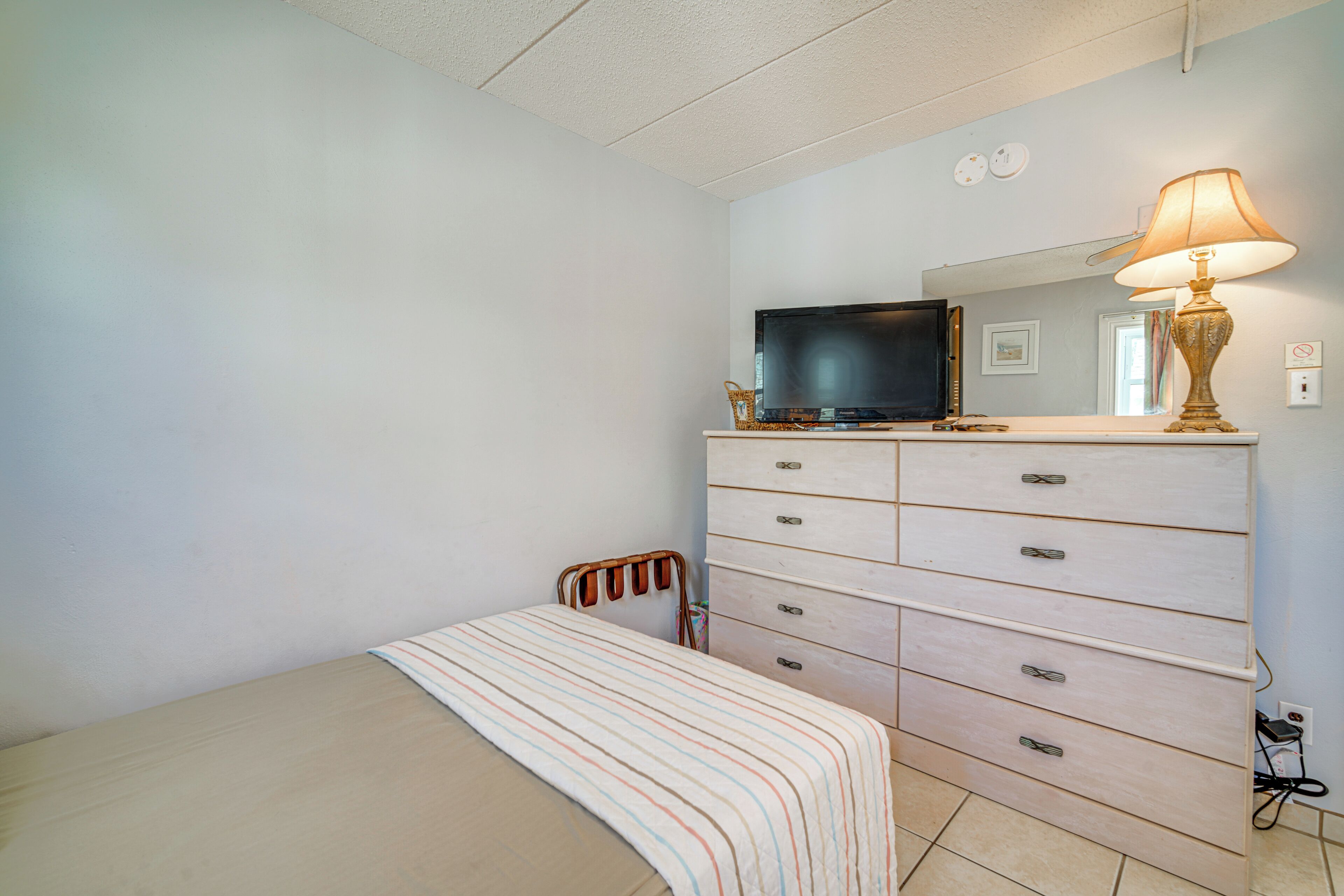 A bedroom with a bed, a dresser, a television, and a lamp.