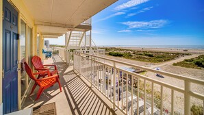 Ein Balkon mit Blick auf den Strand, eine blaue Tür und rote Stühle.
