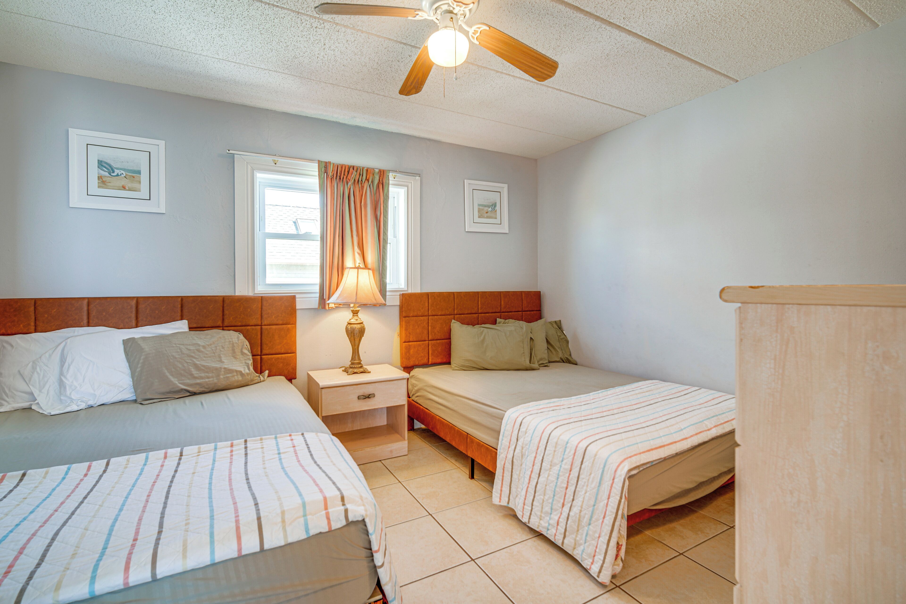 A bedroom with two beds, a nightstand, a ceiling fan, and a window with curtains.
