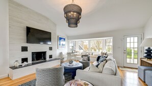 A modern living room with a flat-screen TV, fireplace, comfortable seating, and large windows. - Stunning Westhampton Beach Home w/ Private Pool (Westhampton Beach)