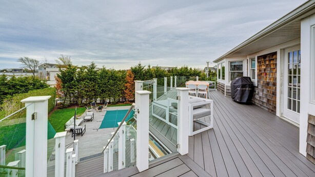 A deck with a glass railing overlooking a swimming pool and a backyard. - Stunning Westhampton Beach Home w/ Private Pool (Westhampton Beach)