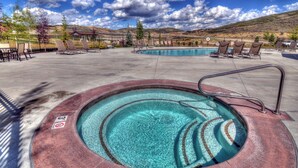 Un área de piscina con sillones de descanso y un jacuzzi, rodeado por una valla y árboles.