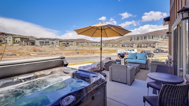 Un jacuzzi en un patio con mobiliario exterior, vista a una zona residencial y cielo despejado.
