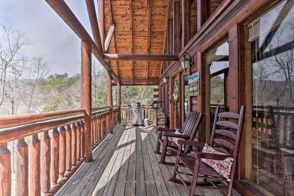 Une terrasse en bois avec une rambarde, un barbecue et deux fauteuils à bascule.