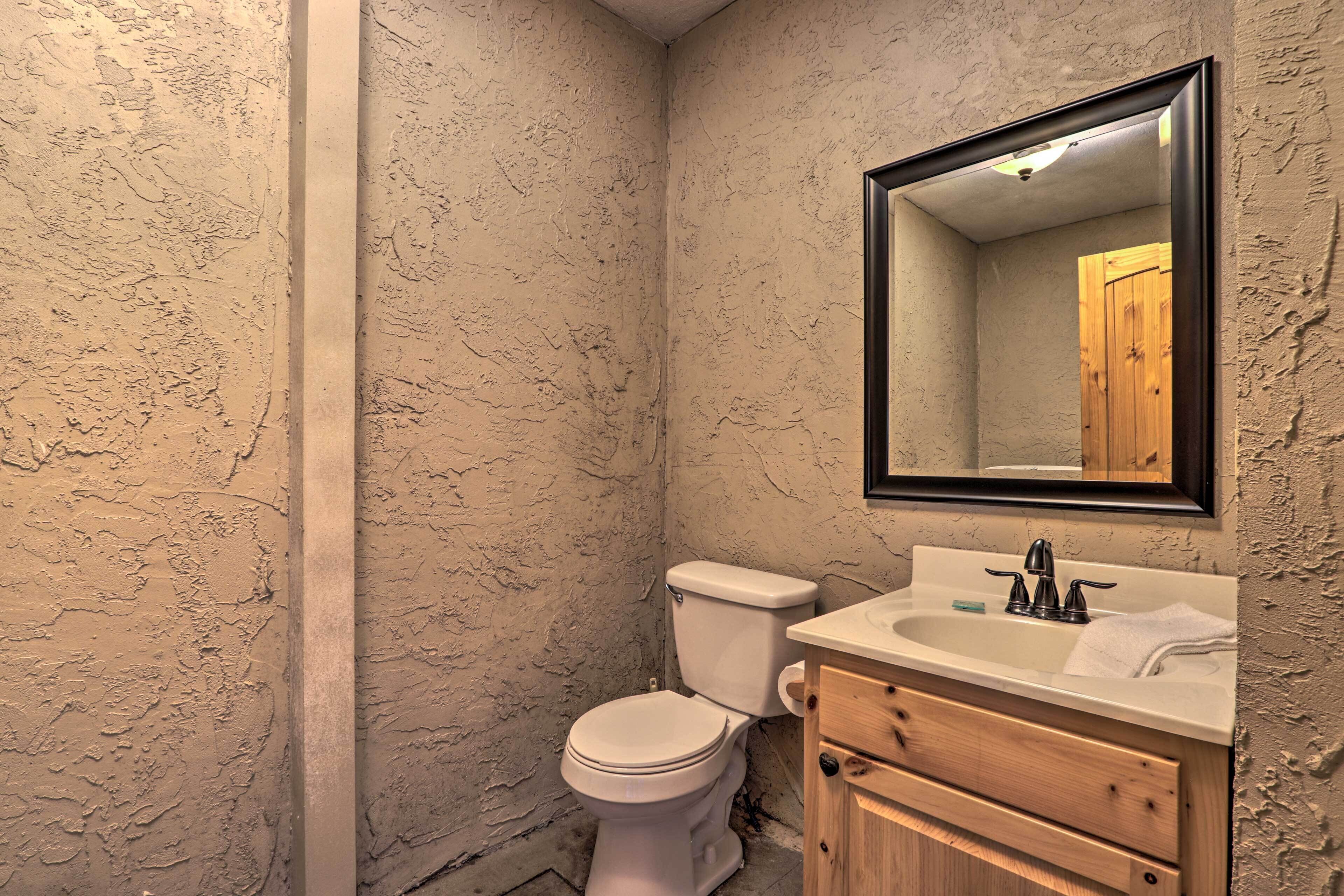 A bathroom with a textured wall, a white toilet, a wooden vanity with a mirror, and a sink.
