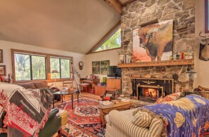 A cozy living room with a stone fireplace, a large window, and a rustic decor. - Riverfront Getaway w/ Treehouse, Fire Pit & Deck! (Mammoth Spring)