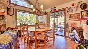 Un coin repas rustique avec une table et des chaises en bois, un lustre et une grande fenêtre donnant sur les arbres.