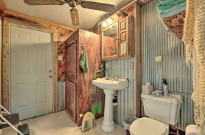 A bathroom with a wooden door, a white sink, a toilet, and a ceiling fan.