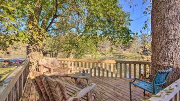 Une terrasse en bois avec des bancs et une table, donnant sur une étendue d’eau et entourée d’arbres.