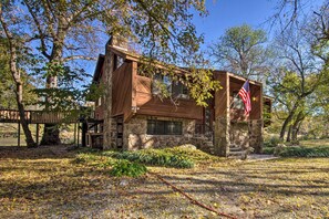 A rustic cabin with a stone foundation and wooden exterior, surrounded by trees and a clear sky. - Riverfront Getaway w/ Treehouse, Fire Pit & Deck! (Mammoth Spring)