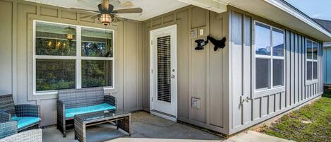 A covered porch with wicker furniture, a ceiling fan, and a door with a metal grill.