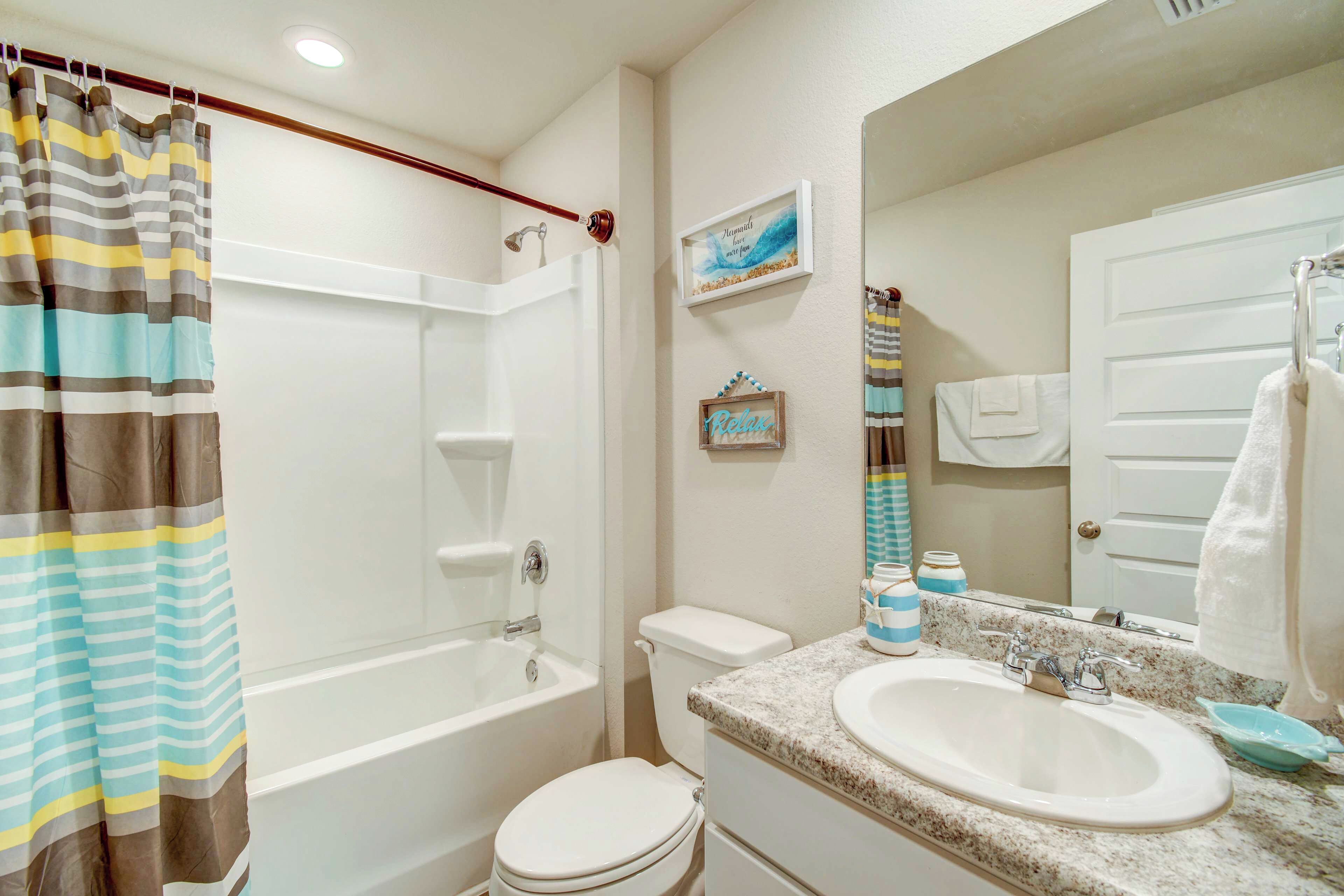 A bathroom with a shower, toilet, sink, and a mirror.