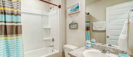 A bathroom with a shower, toilet, sink, and a mirror.