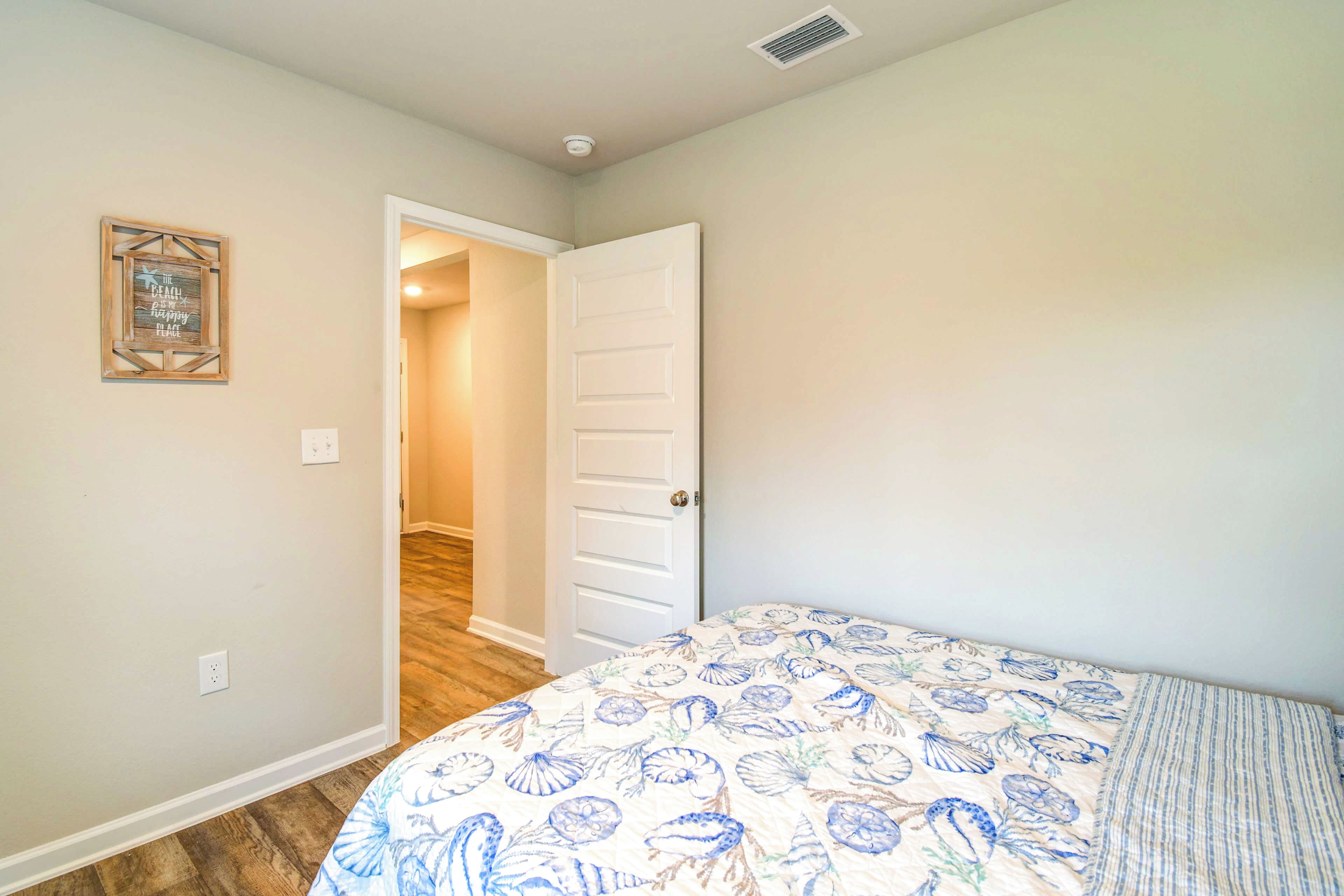 A bedroom with a bed, a door leading to another room, and a wall-mounted light switch.