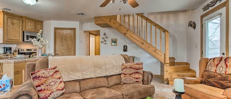 A spacious living room with a brown leather sofa, a wooden coffee table, and a staircase leading to an upper floor.