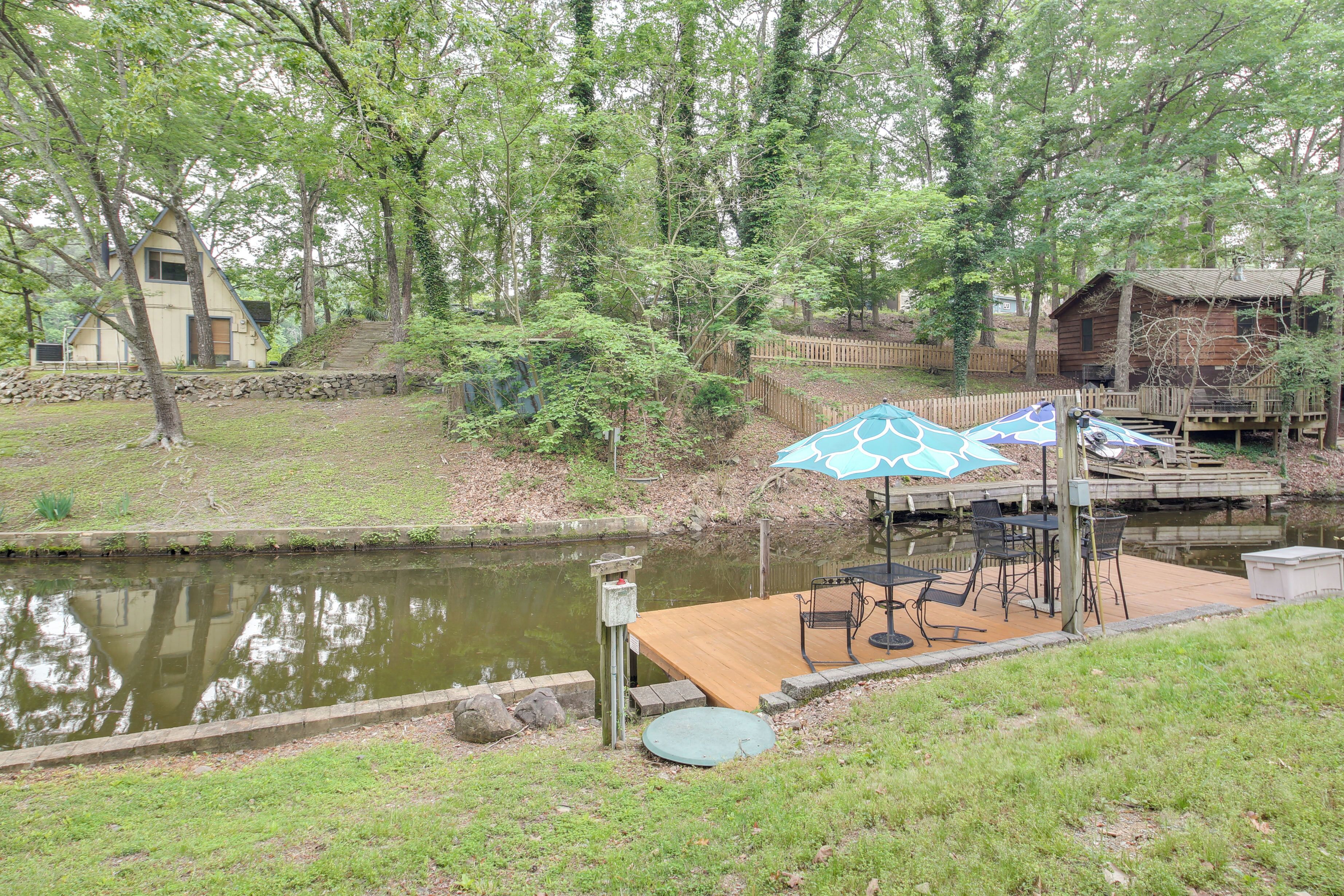 A lakeside cabin with a wooden deck, outdoor seating, and a dock extending into the water.