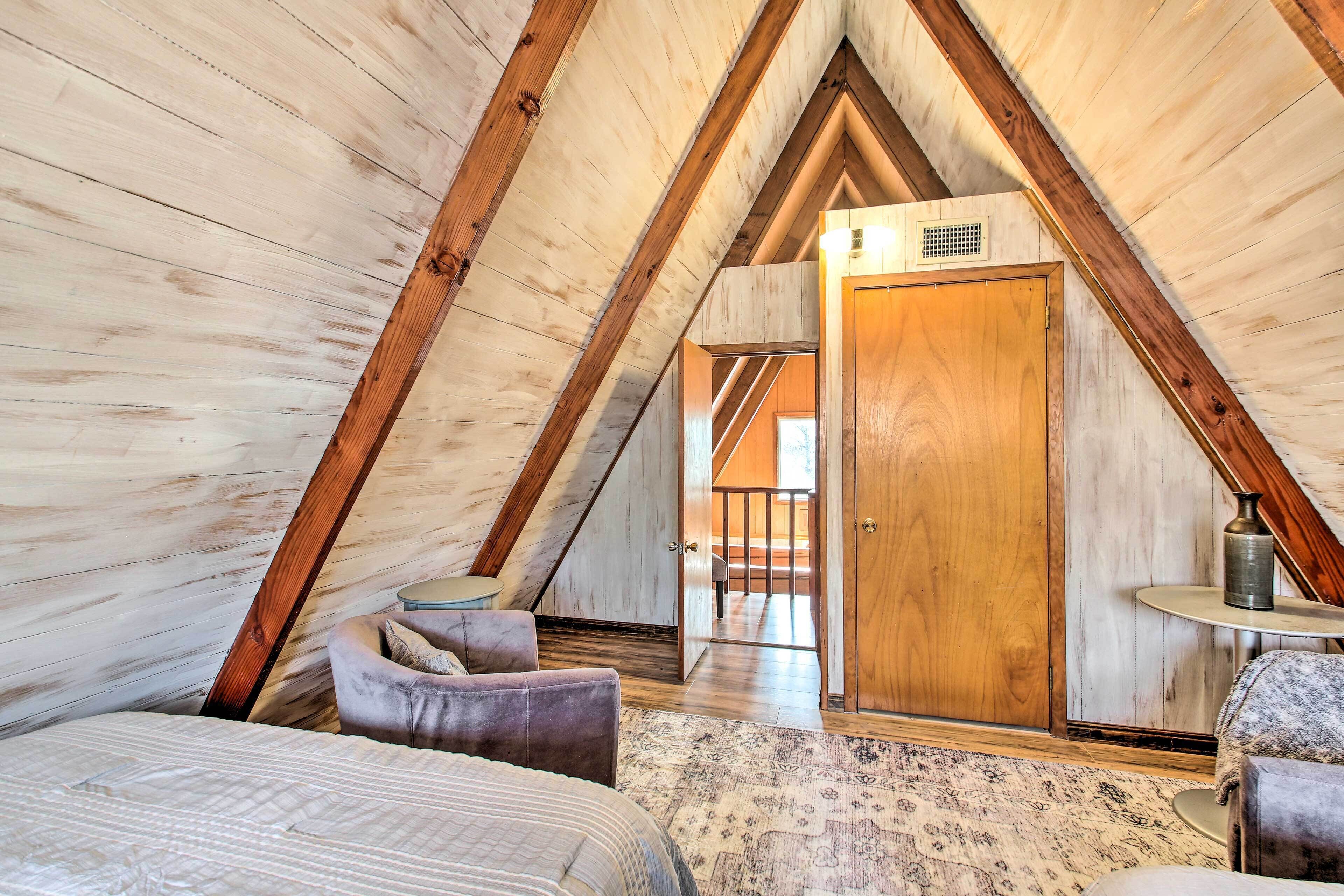 A cozy attic bedroom with a sloped ceiling, a wooden door, a small round table, and a plush chair.