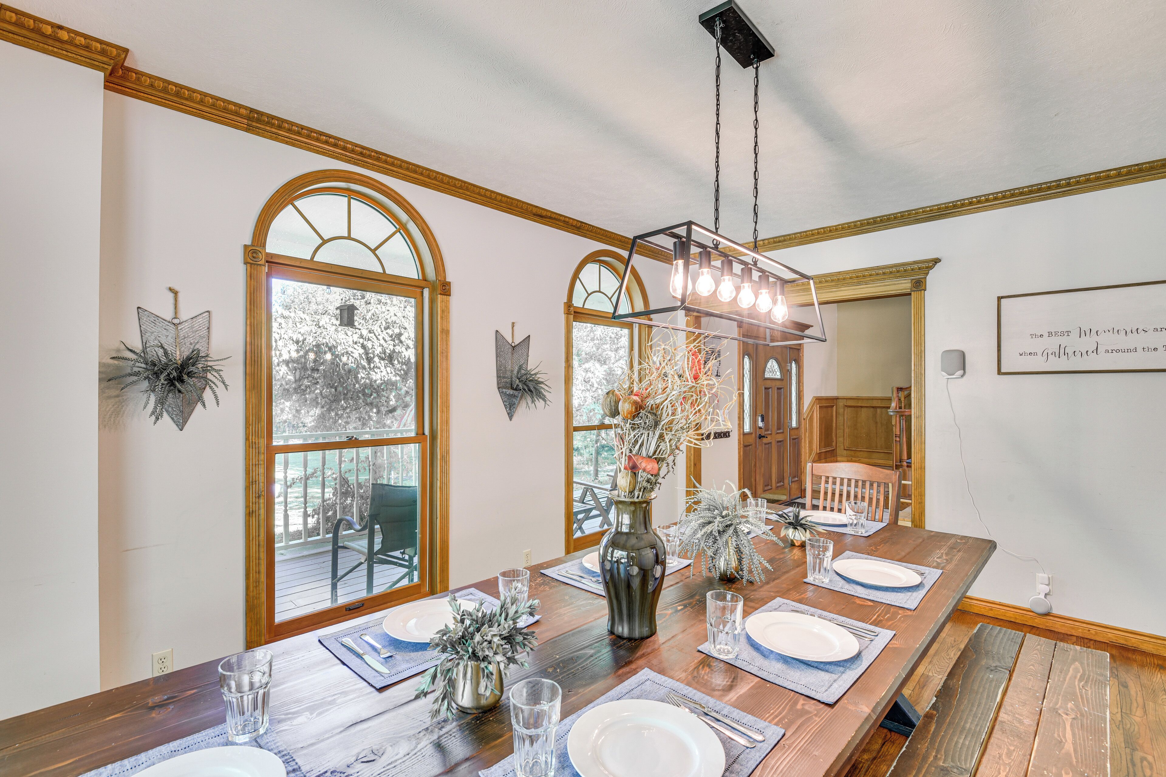 Comedor con una larga mesa de madera preparada para cuatro personas, amplias ventanas arqueadas y una araña.