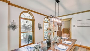 A dining room with a long wooden table set for four, large arched windows, and a chandelier. - Huge Family Home w/ Pool - 13 Mi to Lake Michigan! (La Porte)
