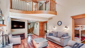 A spacious living room with a high ceiling, wooden staircase, and a cozy seating area with a sofa and armchairs. - Huge Family Home w/ Pool - 13 Mi to Lake Michigan! (La Porte)