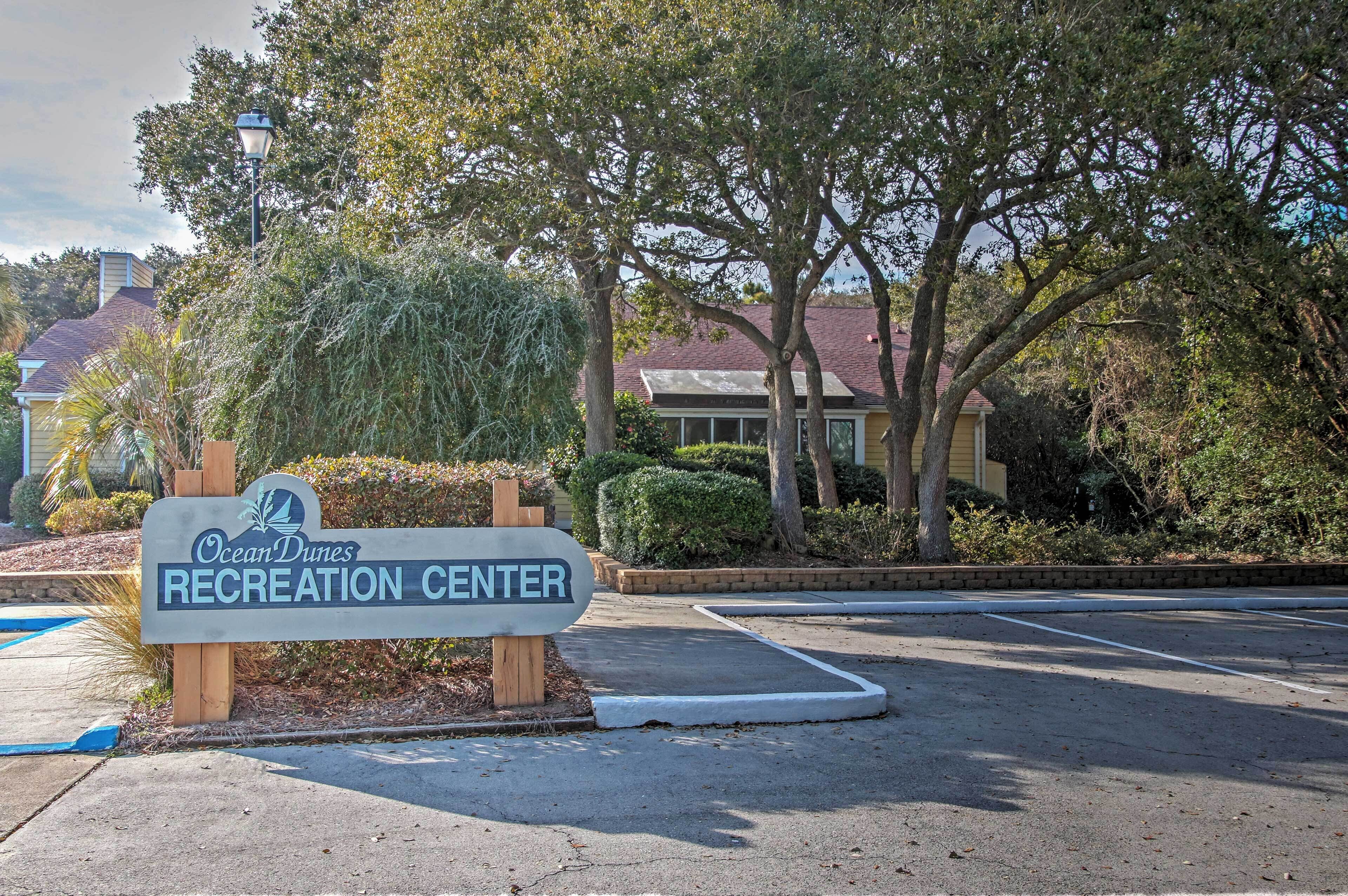 A sign for OceanDunes Recreation Center with a parking lot and trees in the background.
