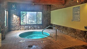 Zona de spa con pared de piedra, una ventana, una bañera de hidromasaje y un cartel con las normas del spa.