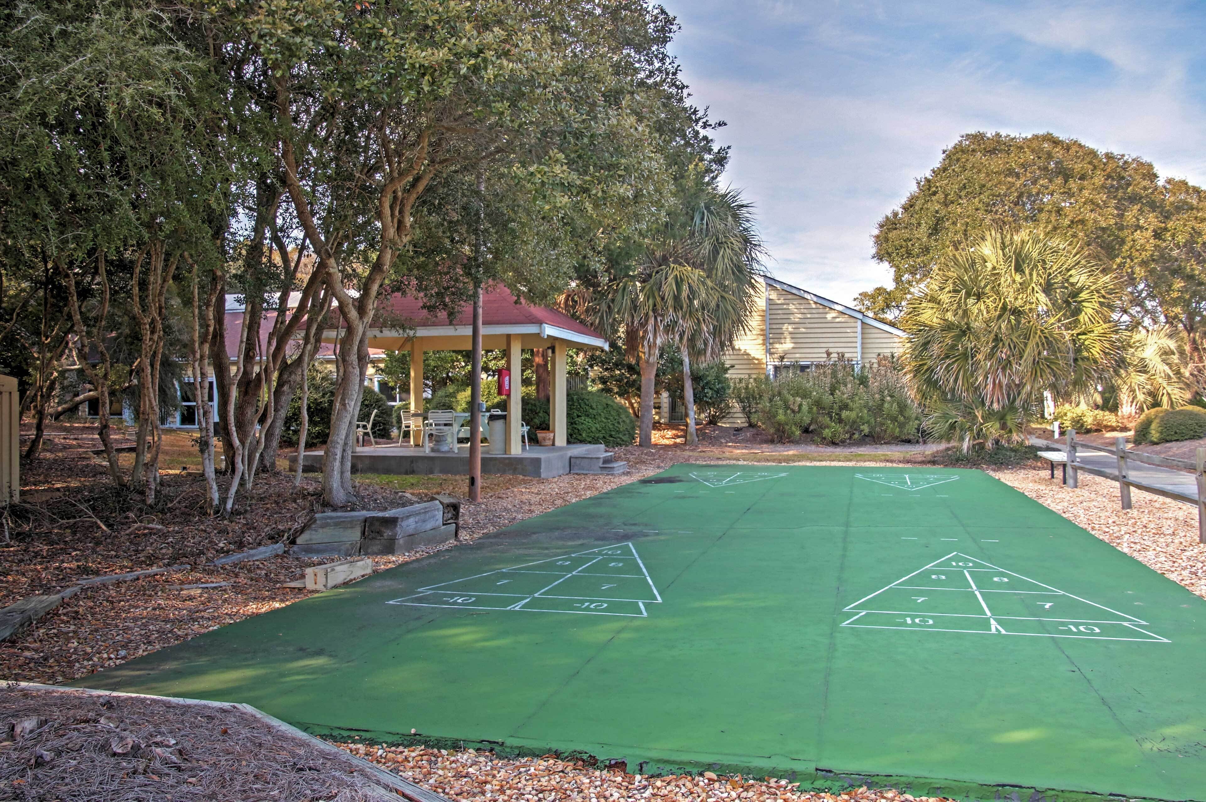 A green shuffleboard court with a gazebo and trees in the background.