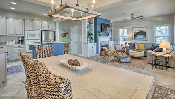 A modern kitchen with white cabinets, a dining area with a woven chair, and a living room with a sofa and a TV.
