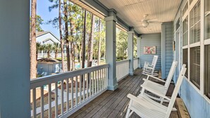 A covered porch with white railings, wooden chairs, and a view of a pool and trees.