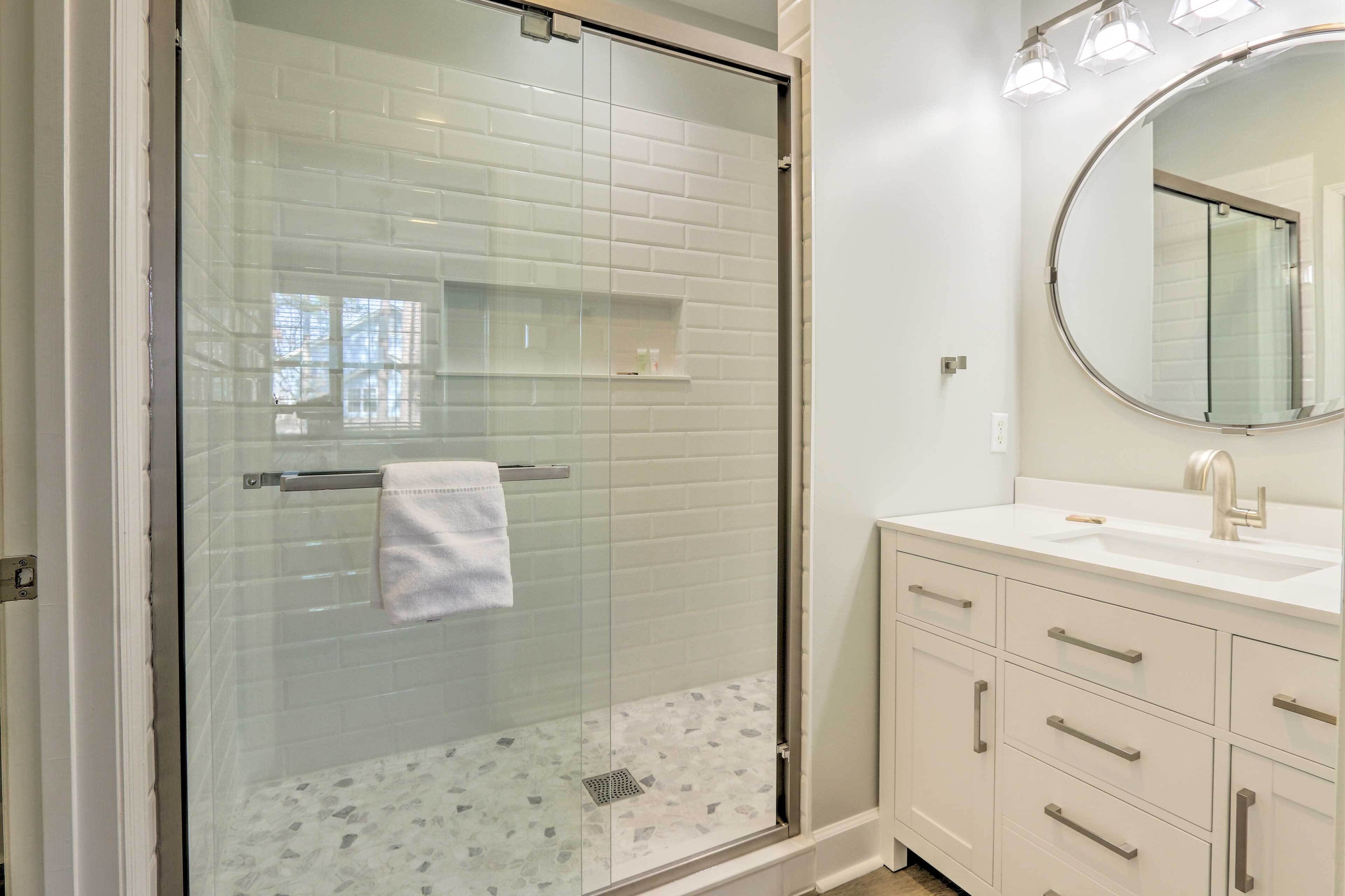 A bathroom with a glass-enclosed shower, a white sink, and a mirror.