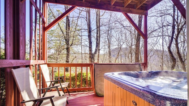 En træterrasse med jacuzzi, stole og udsigt til træer.