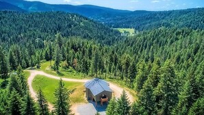 Eine abgelegene Holzhütte, umgeben von dichtem Wald, mit blauem Himmel und Bergen in der Ferne.