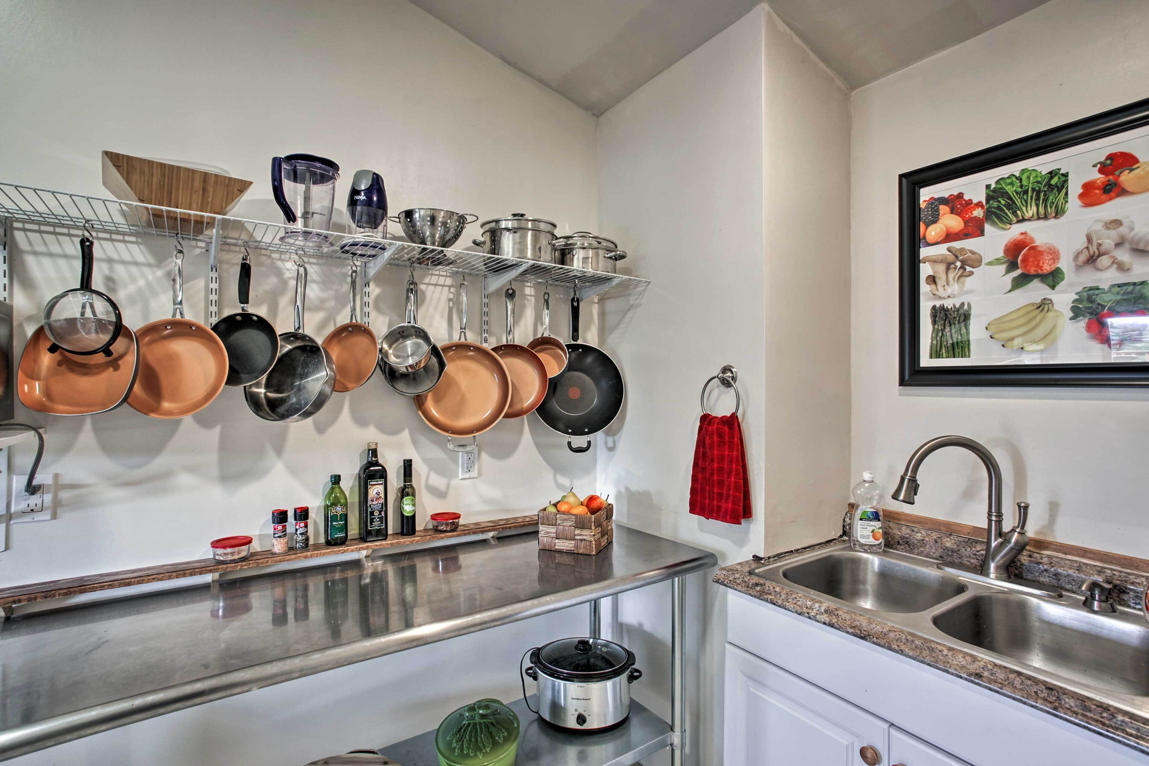 A kitchen with stainless steel countertops, hanging pots and pans, a red towel, and a framed picture of vegetables.