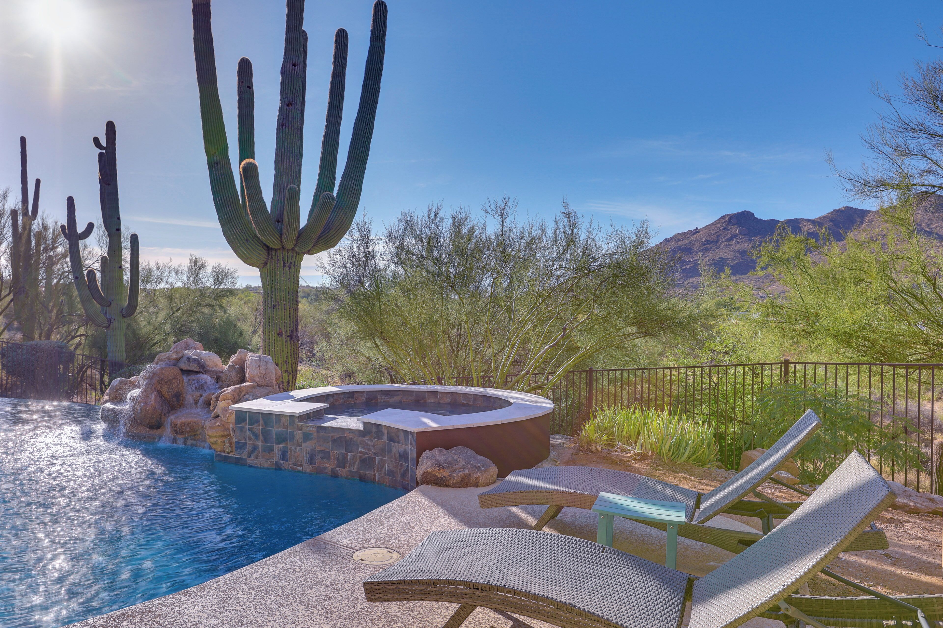 A pool area with lounge chairs, a hot tub, and cacti in a desert landscape.