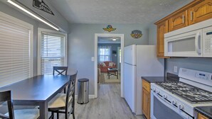 A kitchen with a stove, microwave, and cabinets. There is a dining table with chairs and a trash can.