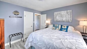 A bedroom with a bed, a wall-mounted coat rack, a door, and a lamp.