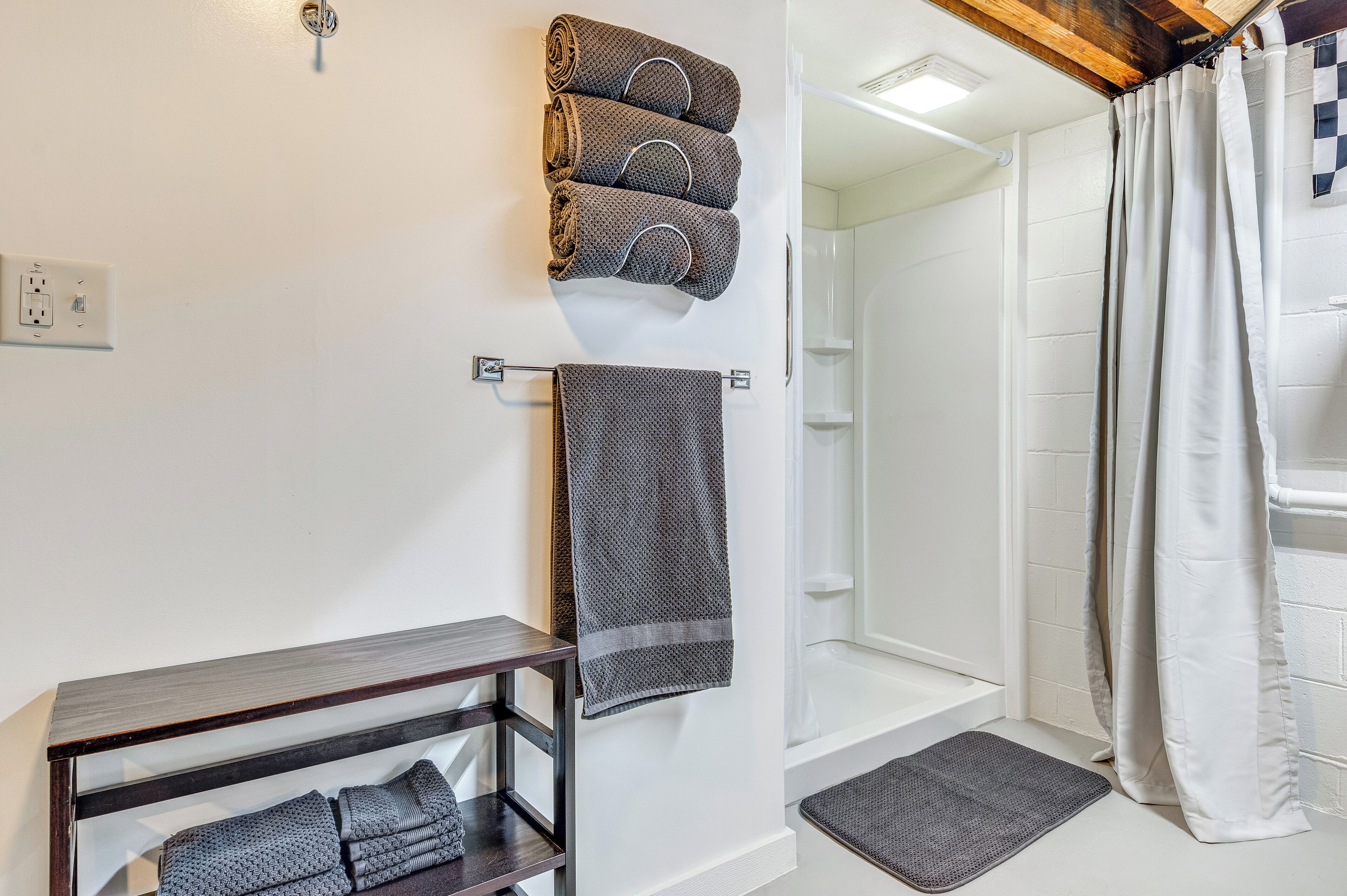 Une salle de bain avec une douche, un porte-serviettes avec des serviettes et une étagère en bois où sont pliées des serviettes.