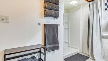 Une salle de bain avec une douche, un porte-serviettes avec des serviettes et une étagère en bois où sont pliées des serviettes.