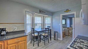 A kitchen with a dining table, chairs, a coffee maker, and a trash can.