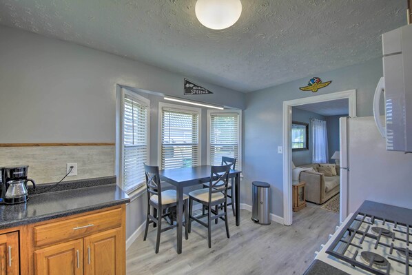 A kitchen with a dining table, chairs, a coffee maker, and a trash can. - Peaceful Speedway Retreat Near Downtown Indy (Indianapolis)