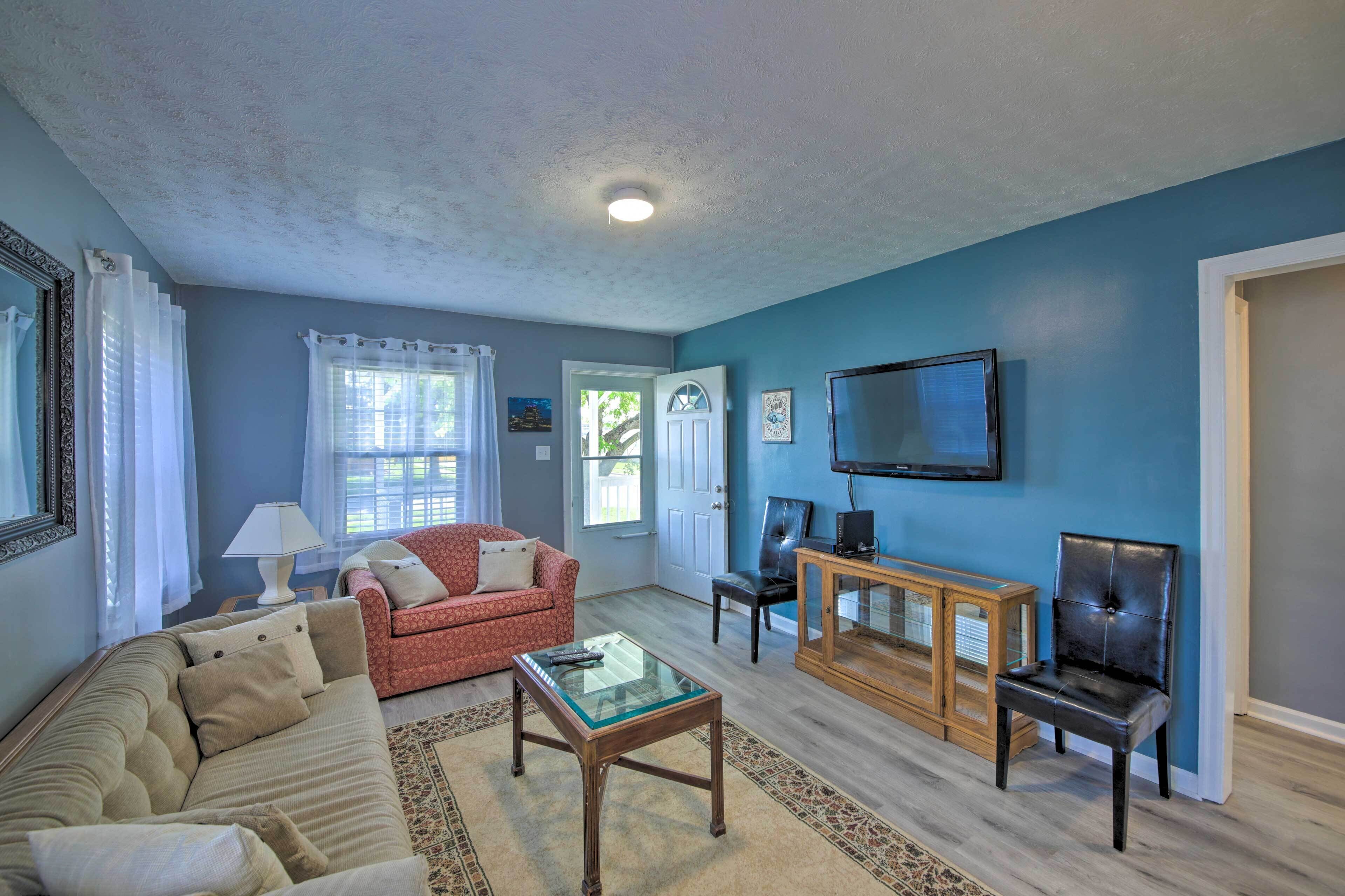 A living room with a blue wall, a red sofa, a glass coffee table, and a TV on a wooden stand.