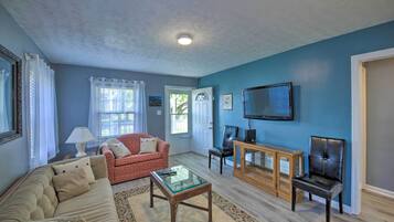 Una sala de estar con pared azul, sofá rojo, una mesa de centro de vidrio y un televisor sobre un mueble de madera.