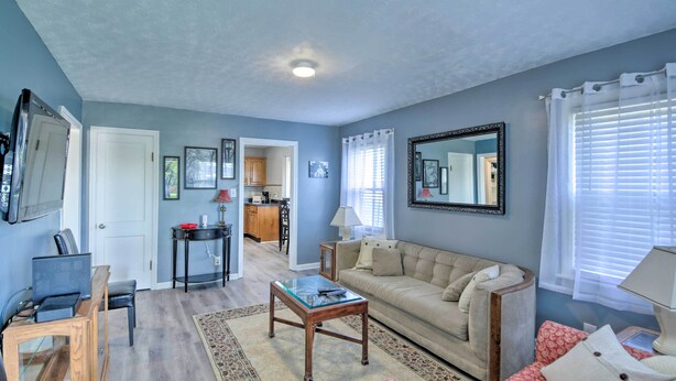 A living room with a sofa, armchairs, a coffee table, and a TV. There is a kitchen area in the background.