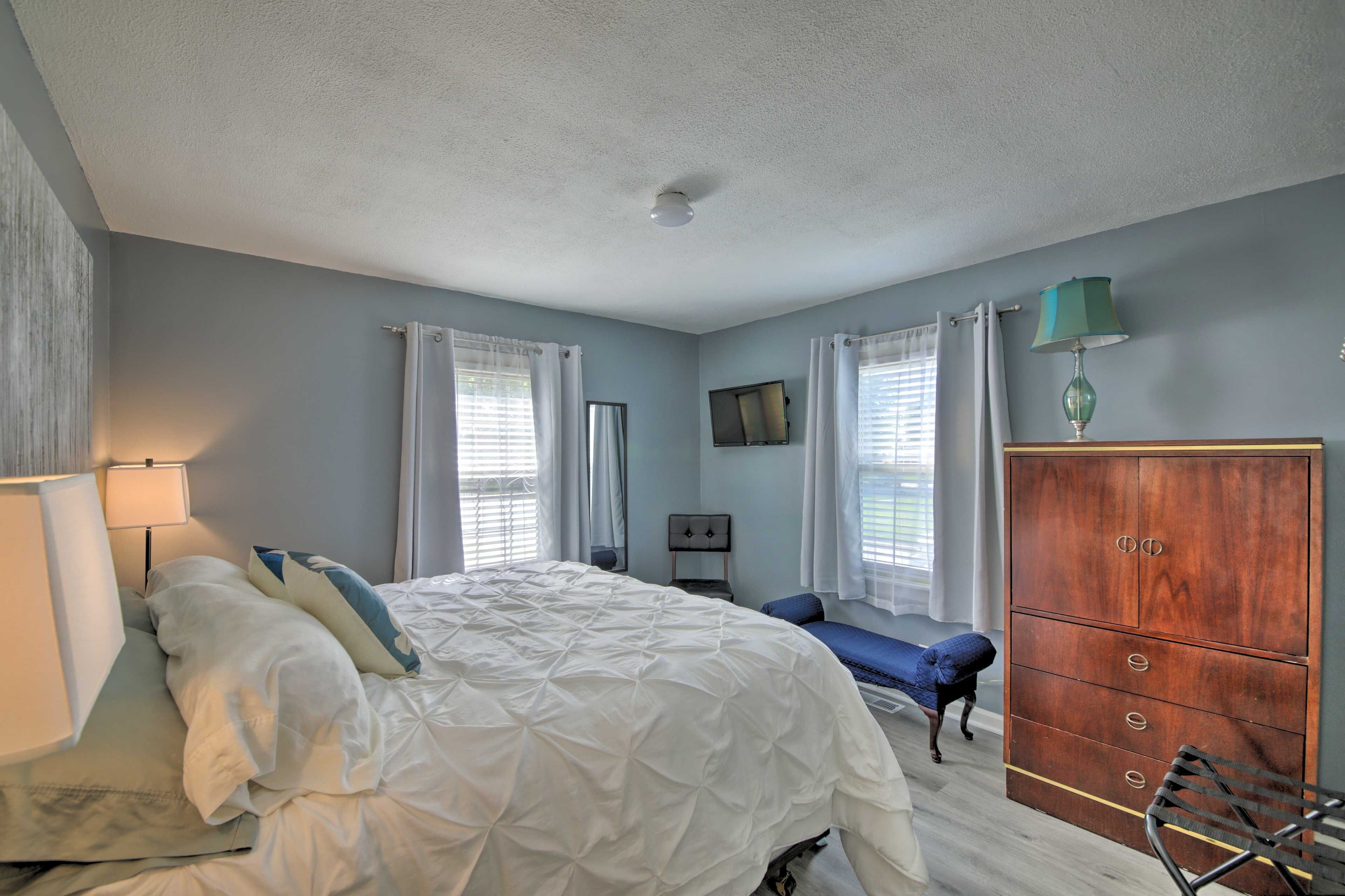 A bedroom with a bed, a dresser, a chair, a TV, and a lamp.