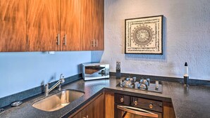 A modern kitchen with wooden cabinets, a stainless steel sink, a microwave, and a decorative wall piece. - Sweet & Chic Puerto Vallarta Condo: Walk to Beach! (Puerto Vallarta)