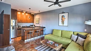 A modern kitchen with wooden cabinets, a central island with bar stools, a green sofa, and a ceiling fan. - Sweet & Chic Puerto Vallarta Condo: Walk to Beach! (Puerto Vallarta)