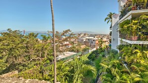 A residential building with balconies, lush greenery, and a view of the city and ocean. - Sweet & Chic Puerto Vallarta Condo: Walk to Beach! (Puerto Vallarta)