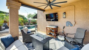 Eine überdachte Terrasse im Freien mit Deckenventilator, einem flachbildfernseher an der Wand, einem Pool und Gartenmöbeln, darunter ein Sofa, ein Stuhl und ein Tisch.