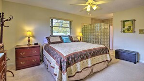 A bedroom with a bed, two bedside tables with lamps, a ceiling fan, a window, a glass partition, and a suitcase.